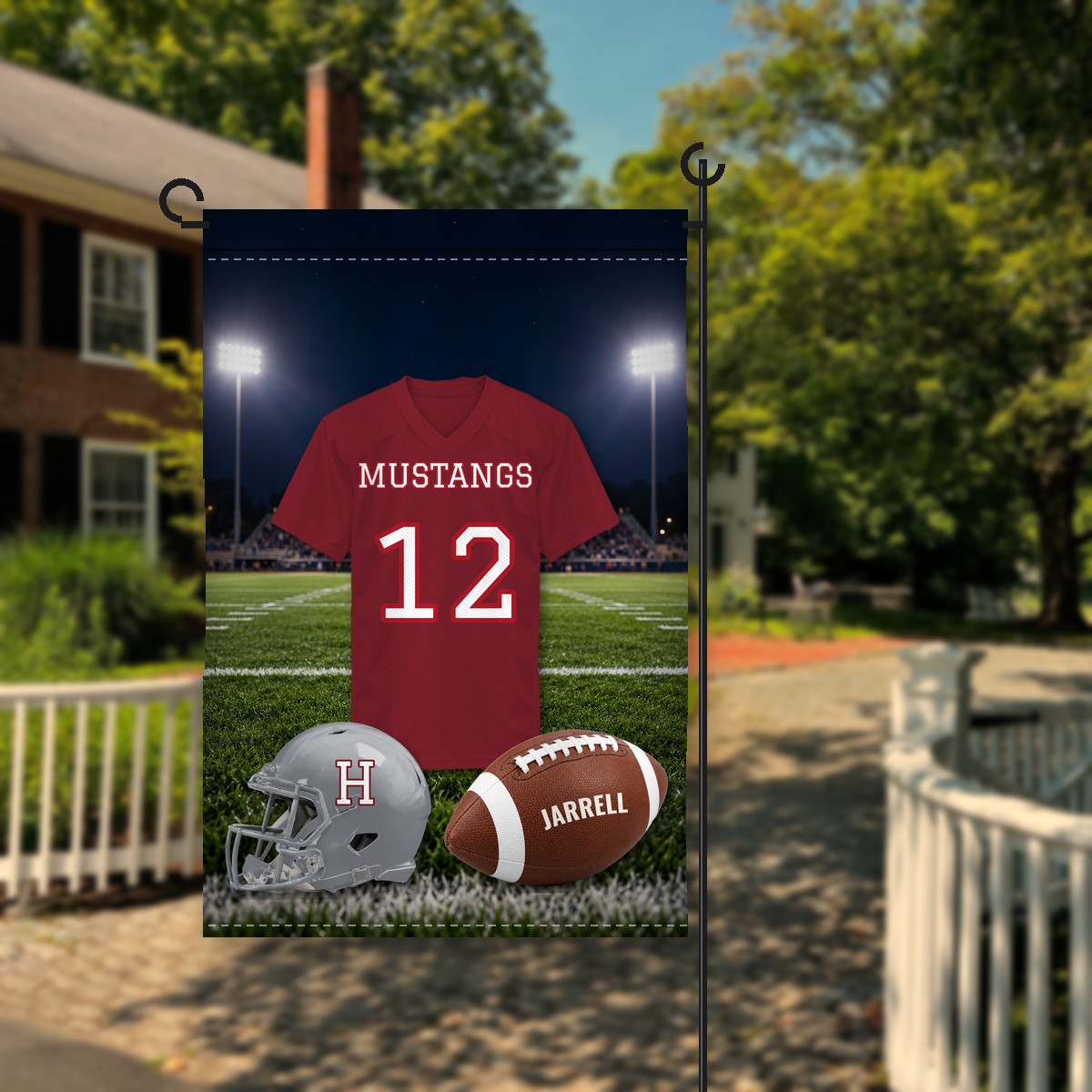 Holmes Mustangs football garden flag in maroon and gray: realistic jersey reading Mustangs 12 under stadium lights, a gray helmet with an H and a football with the name Jarrell, on a stand in front of a house