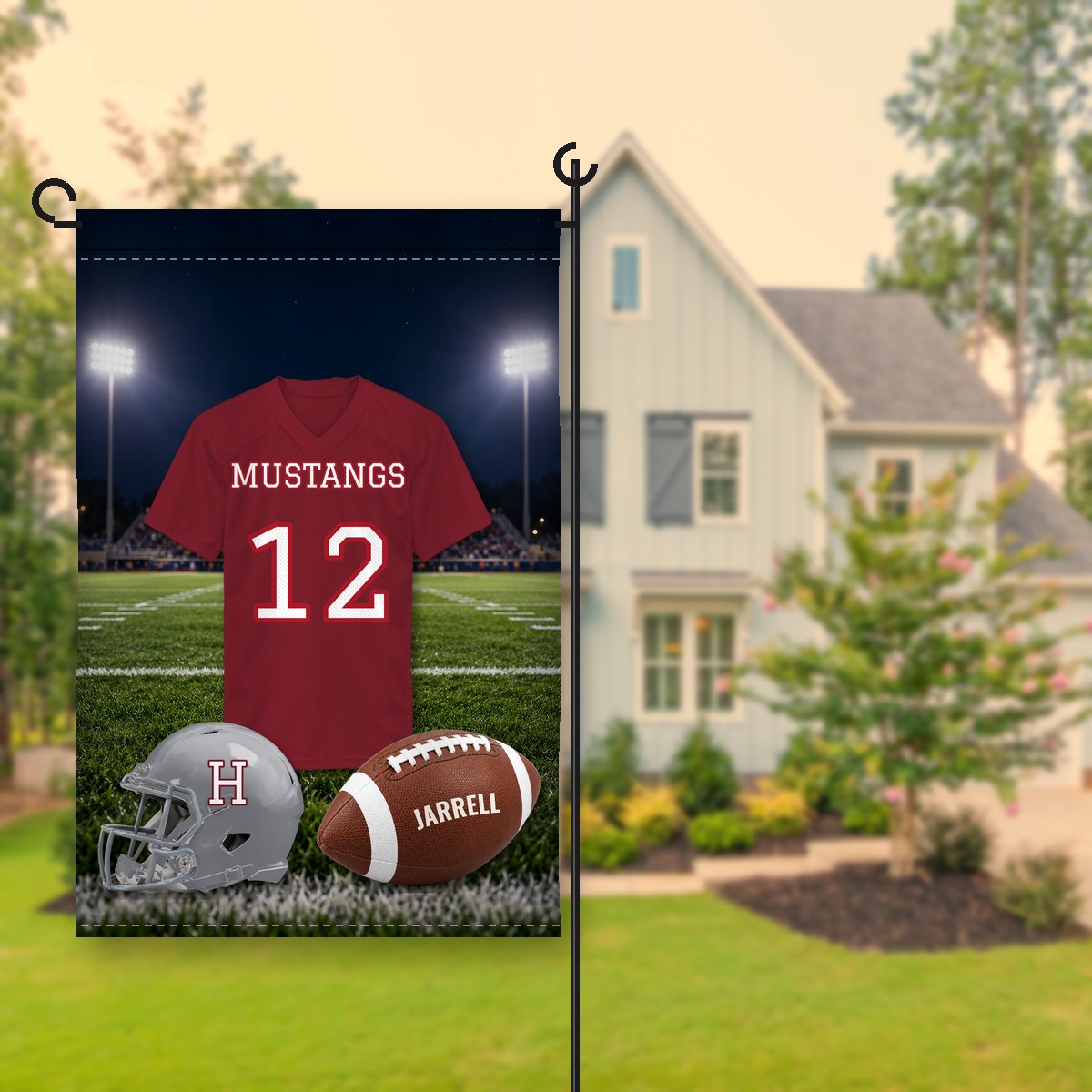 Holmes Mustangs football garden flag in maroon and gray: realistic jersey reading Mustangs 12 under stadium lights, a gray helmet with an H and a football with the name Jarrell, on a stand in front of a house